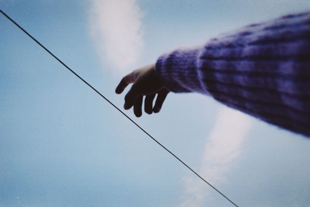 A dramatic shot of a hand reaching up towards the sky with a blue background.