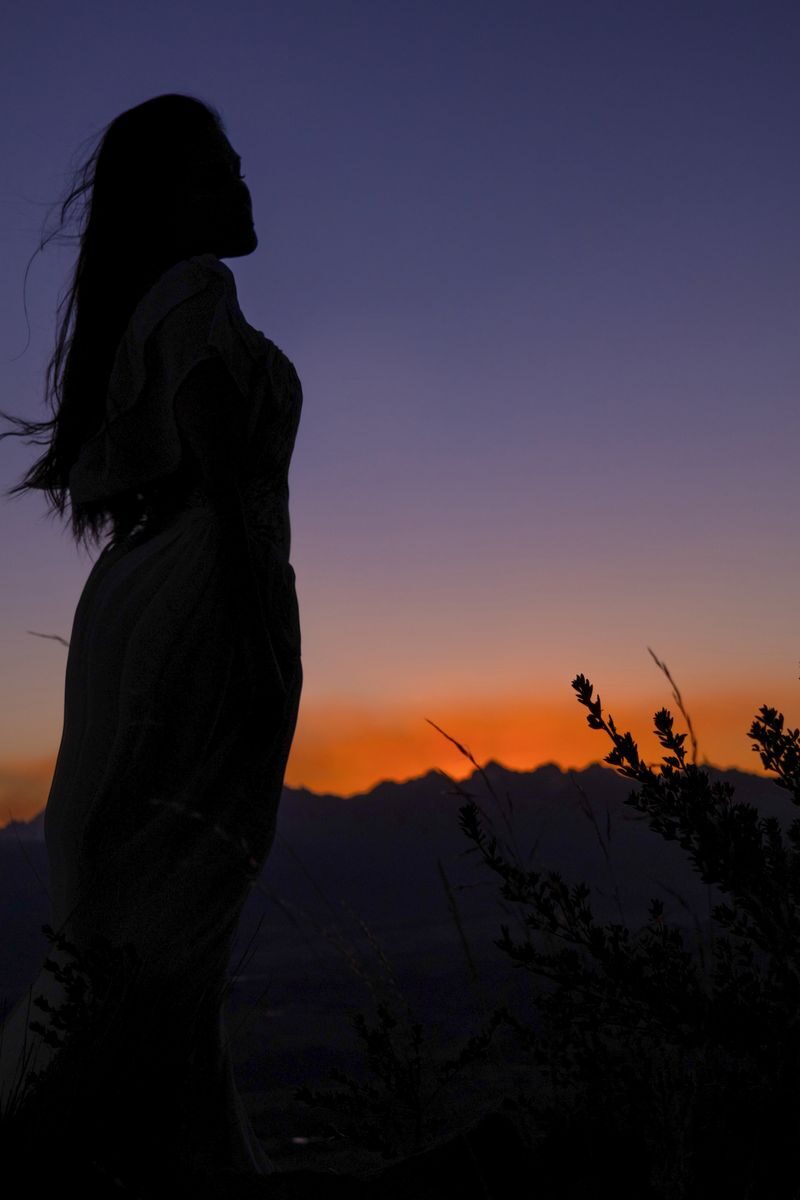 Silueta de una mujer contra un atardecer con montañas, símbolo de mirar hacia dentro