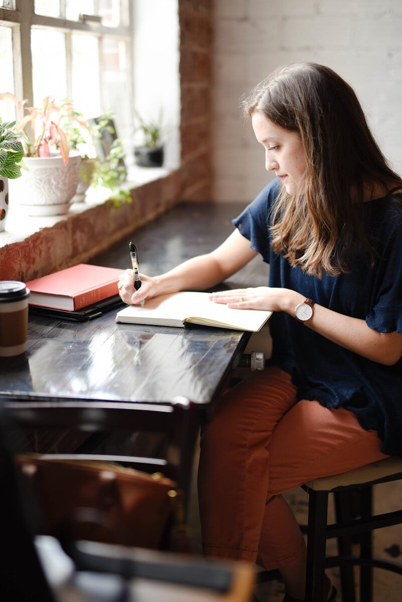 Mujer escribiendo con calma junto a una ventana, en un momento de reflexión creativa