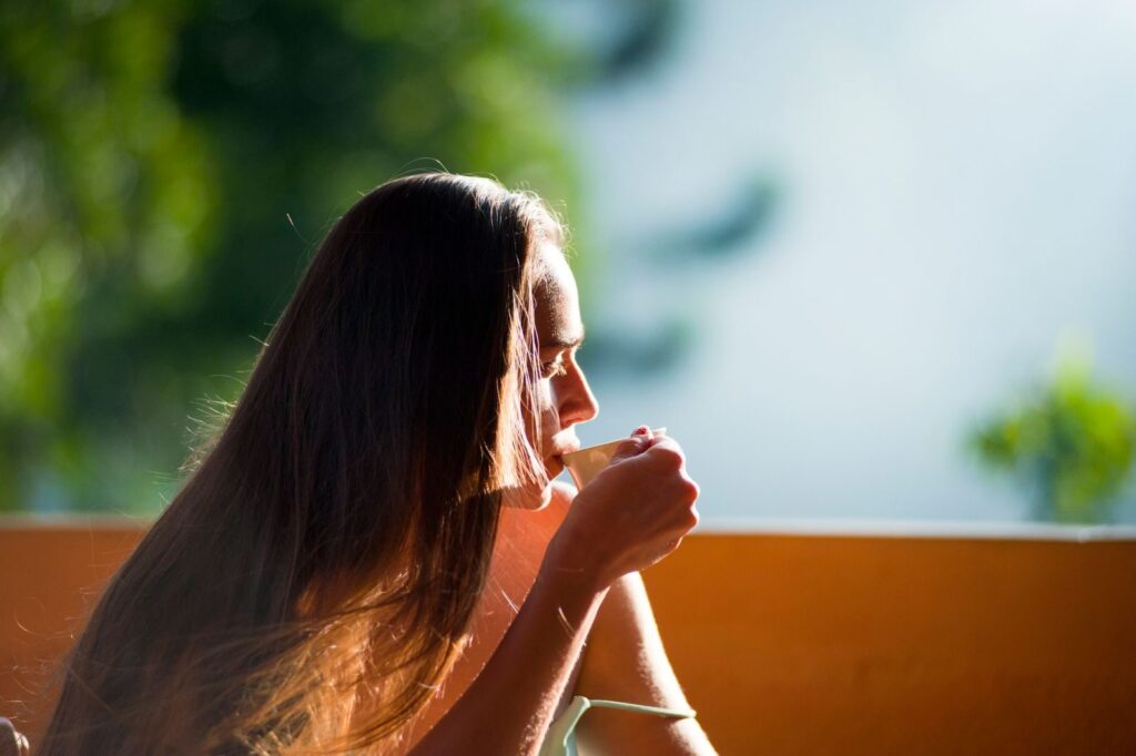 Mujer disfrutando de un té con calma al aire libre por la mañana, en una rutina cuidada y saludable