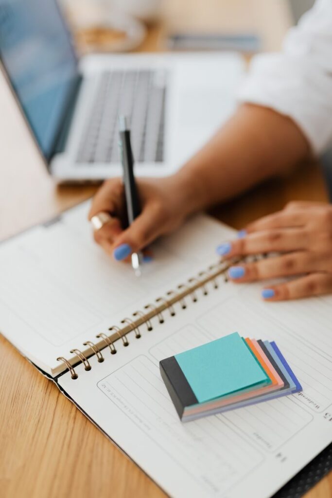 Persona escribiendo notas a mano junto a su portátil, organizando tareas prioritarias