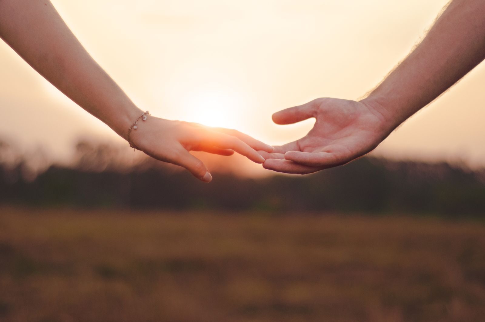 Dos manos entrelazándose al atardecer, símbolo de la relación de pareja.