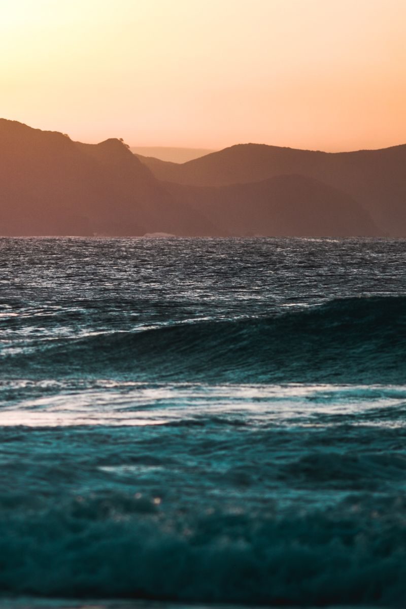 Captivating ocean scene with waves and distant mountains under a stunning sunset.
