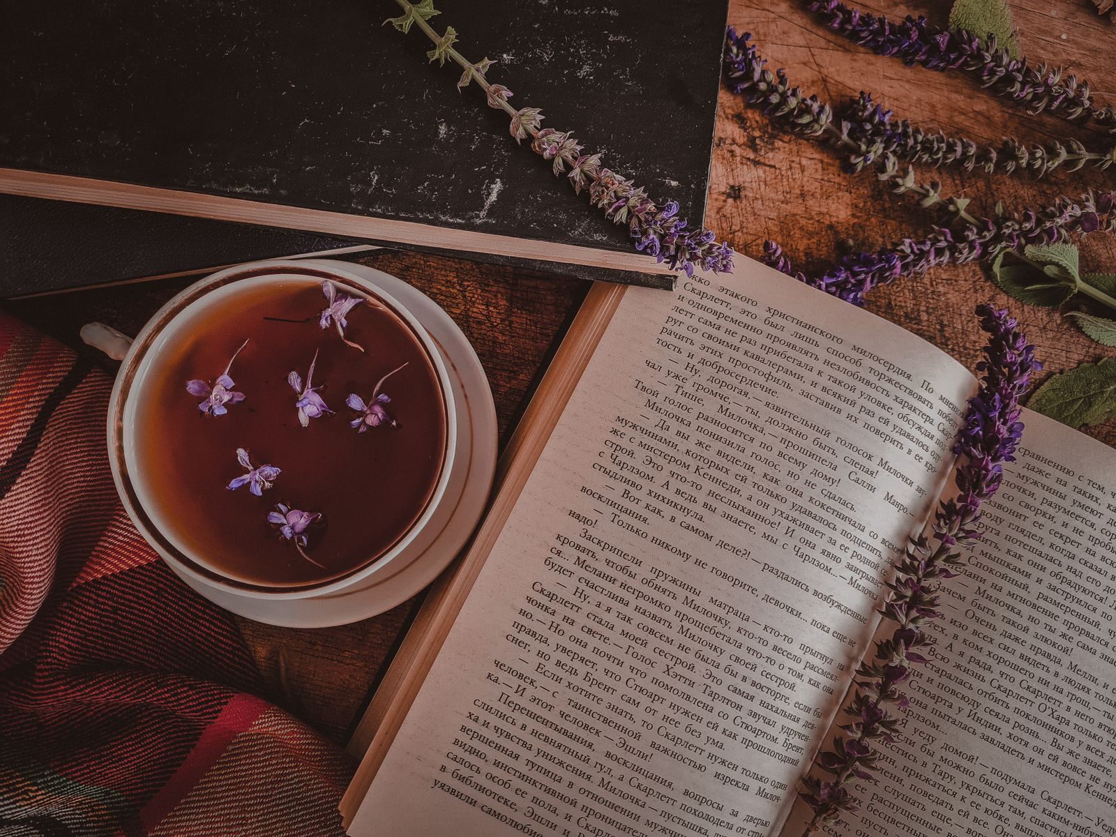 Top view of a cup of tea with violet flowers next to an open book and lavender on a rustic table.