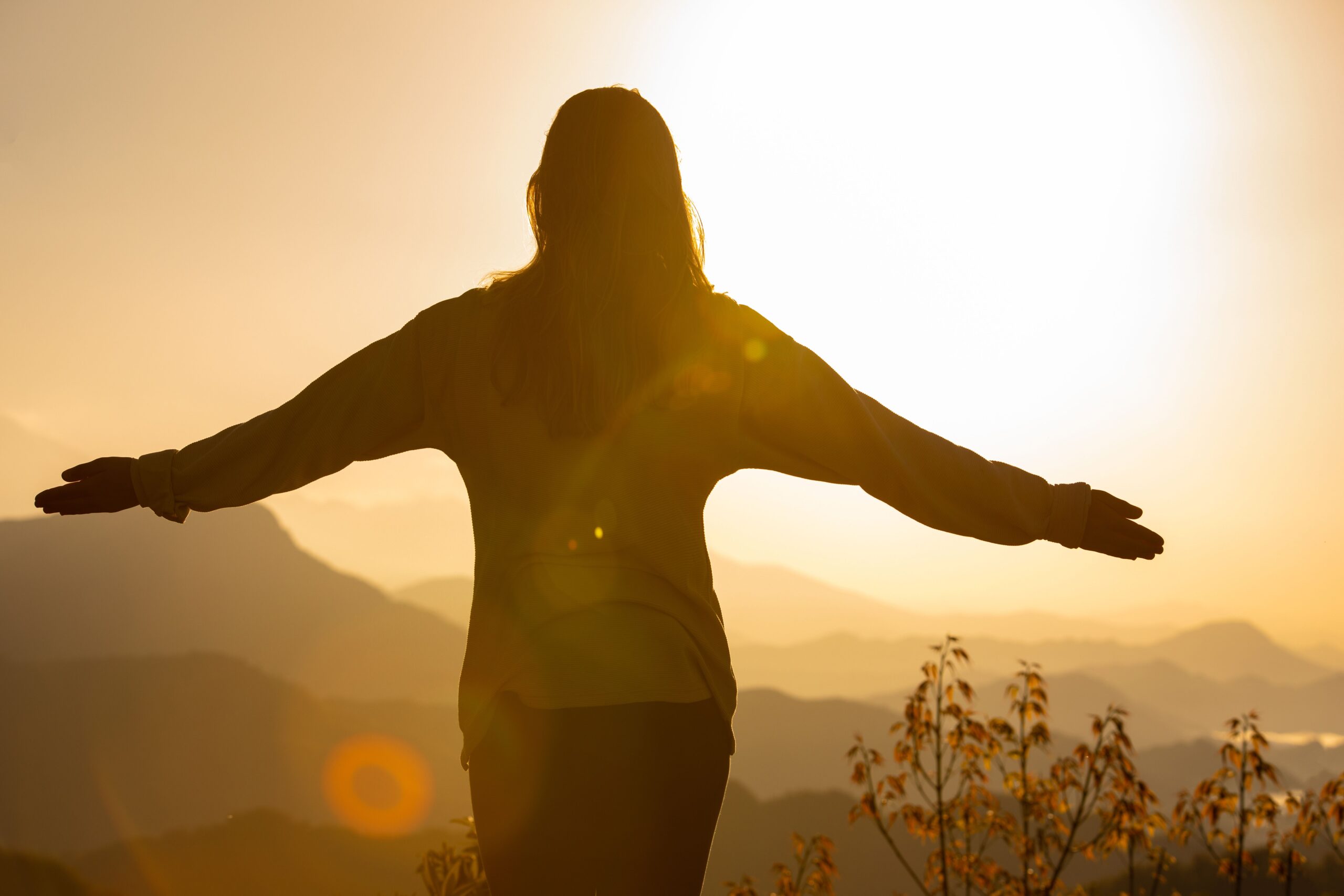Silueta de una mujer con los brazos abiertos frente al amanecer, representando la apertura y la curiosidad que transmite el Ascendente en Géminis