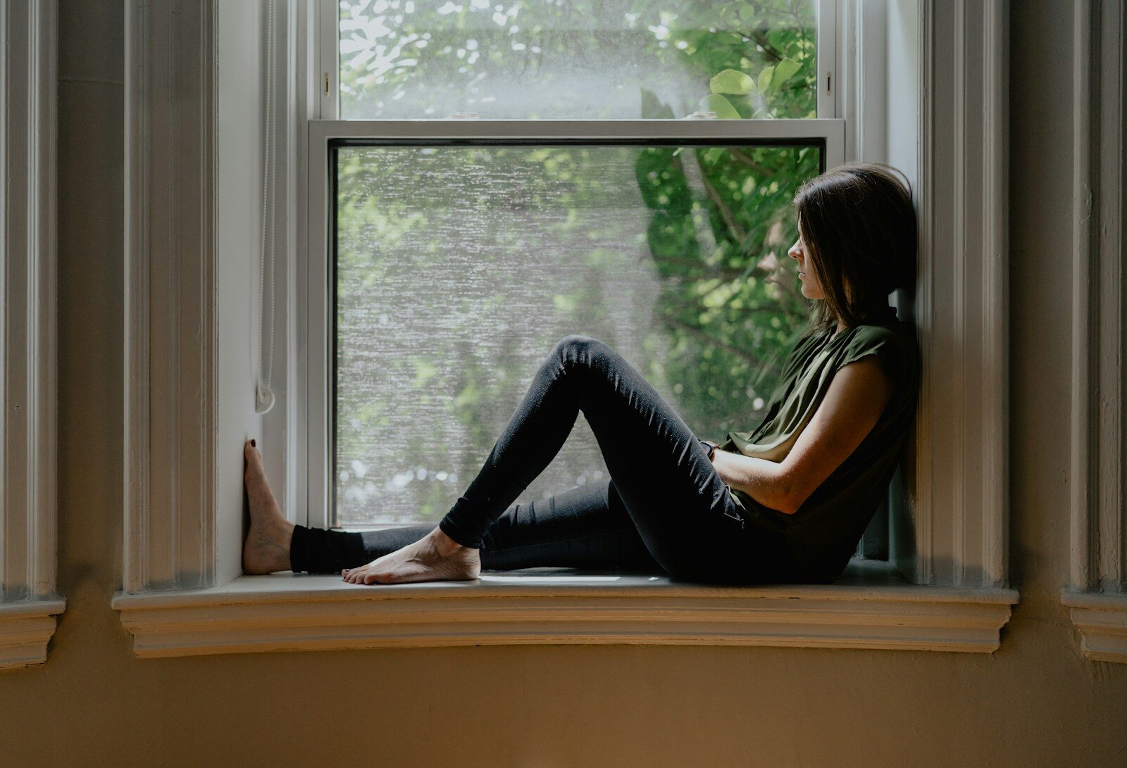 Mujer sentada junto a una ventana en un momento de introspección y autoconocimiento